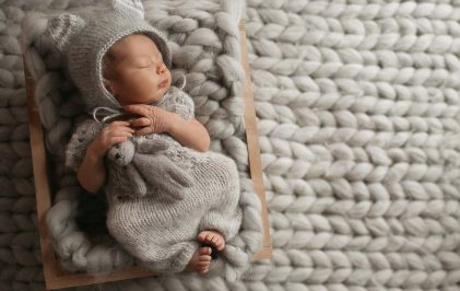 Tiny baby in grey clothes sleeps on woolen blanket